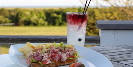 View of Lobster Roll on a White Plate with a Glass of Lemonade on the Outdoor Terrace at The Dunes