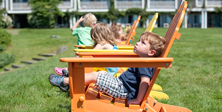 children sitting in rainbow colored adirondack chairs