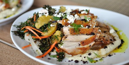 View of Sliced Chicken with Herbs & Field of Greens on a White Plate at The Dunes