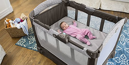 View of Baby Girl Laying in a Gray Pack n Play Portable Crib