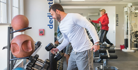 View of Man Using Dumbells & Man Working on Cardio Machines in the Winnetu Fitness Center