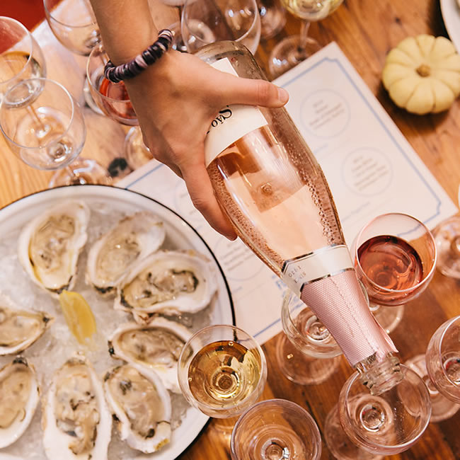 Bottles of Wine Being Poured Into Glasses Together With Oysters on the Half-Shell on White Plates