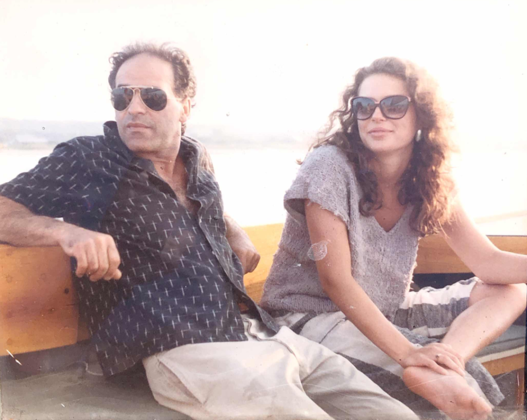 A man and woman in sunglasses sitting on a bench looking to their right