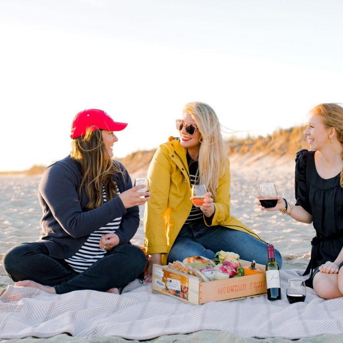 3 women sitting on the beach with drinks in their hands